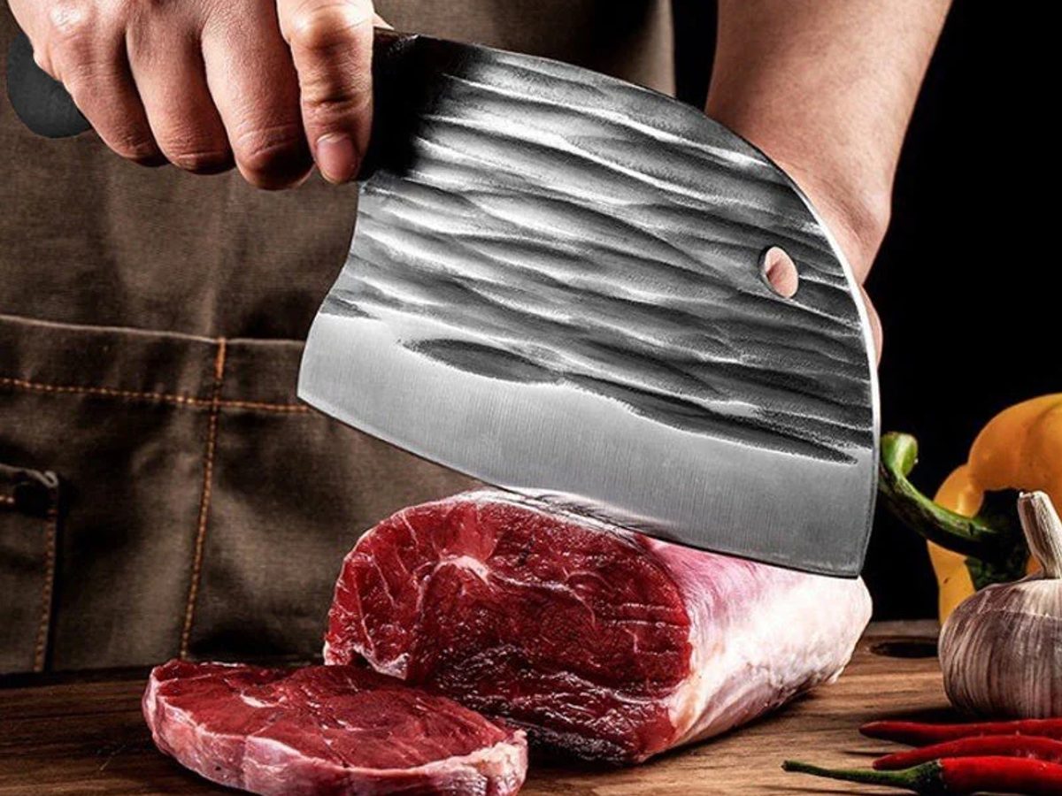 Cuchillo Tazaki de hoja martillada cortando carne sobre una tabla